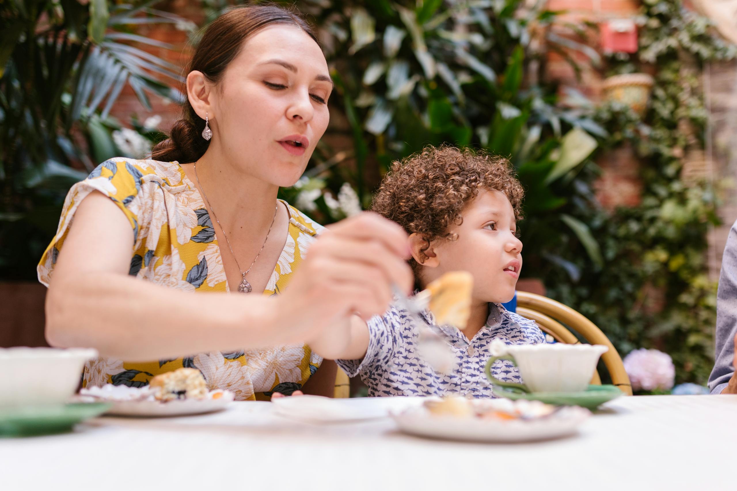A mother and her young son sharing a delightful meal outdoors in a garden setting.